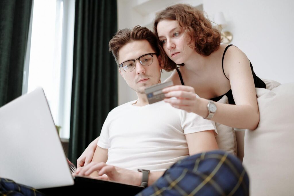 A young couple using a laptop and credit card for online shopping indoors.