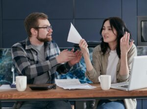 A couple discussing financial paperwork indoors, with a laptop and coffee on the table.