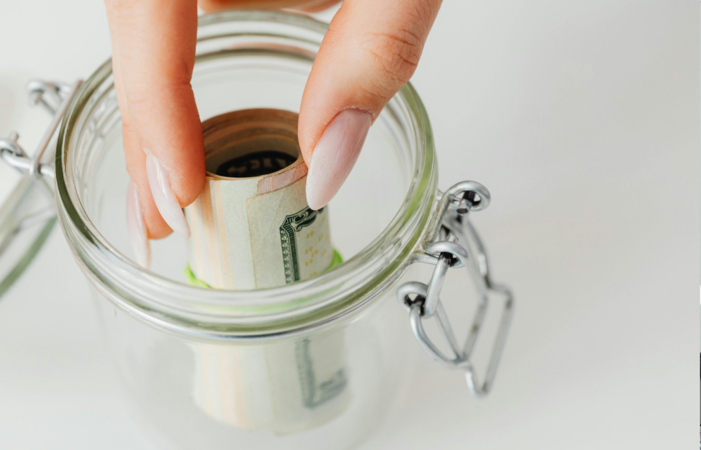 A person adding cash to a savings jar labeled 
