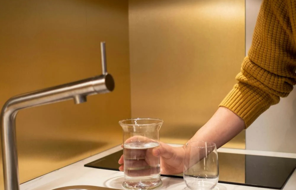 A person filling a glass with water from a kitchen faucet equipped with an under-sink filter