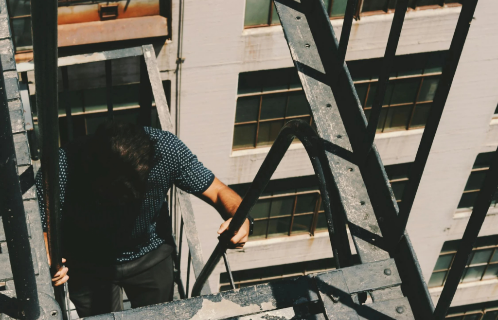 An individual climbing a ladder leaning against a corporate building