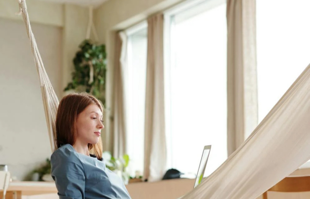 A middle-aged person relaxing on a hammock with a laptop