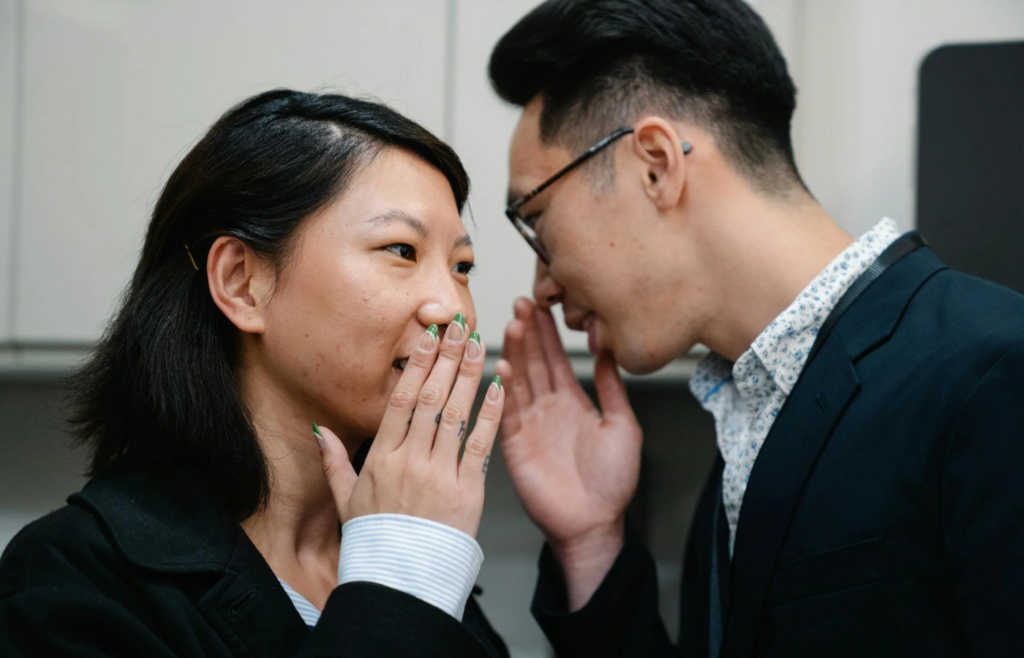 Two colleagues whispering in an office setting