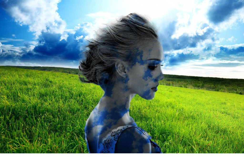 A person in a green field under a blue, cloudy sky