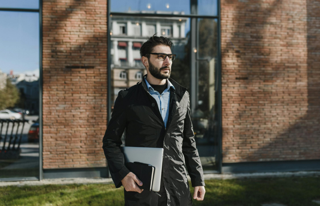Man in glasses holding laptop, walking outside