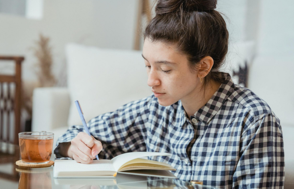 An individual journaling at a desk with a cup of tea