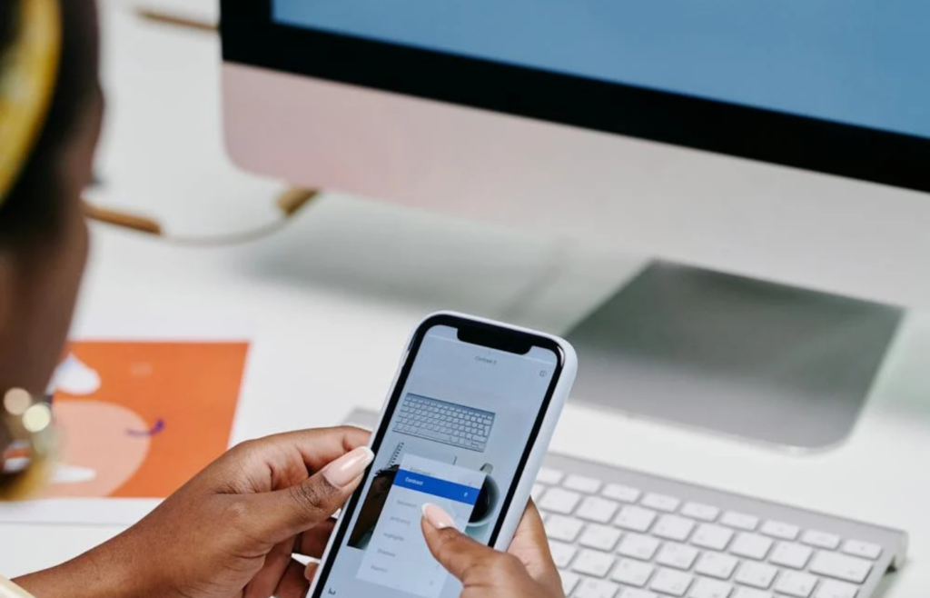 Person using smartphone by computer workstation setup
