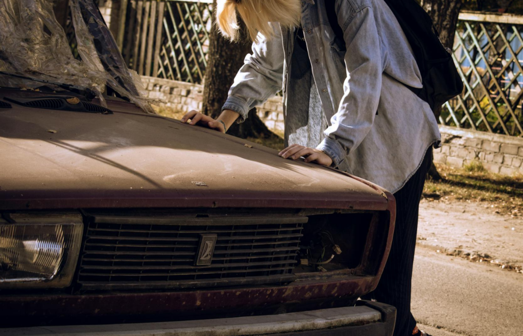 A broken-down car on the roadside with a person looking distressed