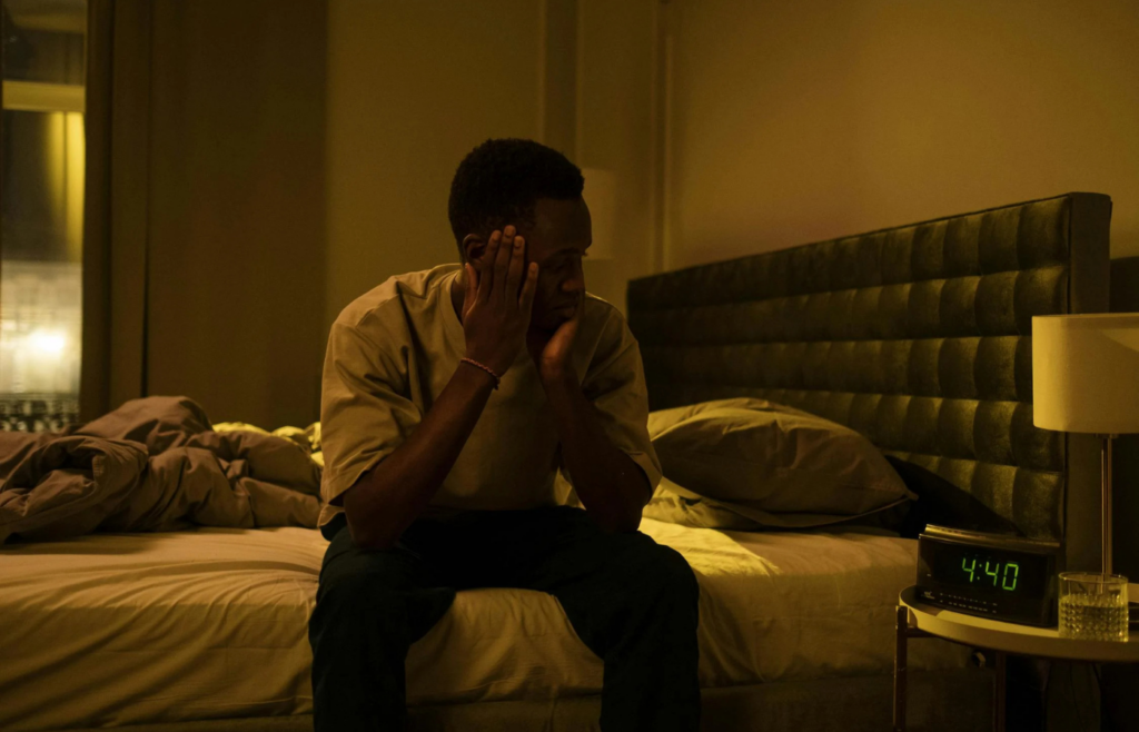 A person rubbing their eyes, looking exhausted, with an alarm clock showing 4:00 AM