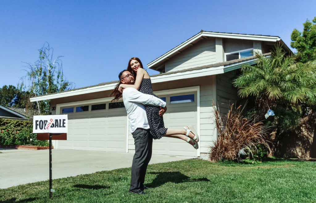 A family standing in front of a new home with a "Sold" sign