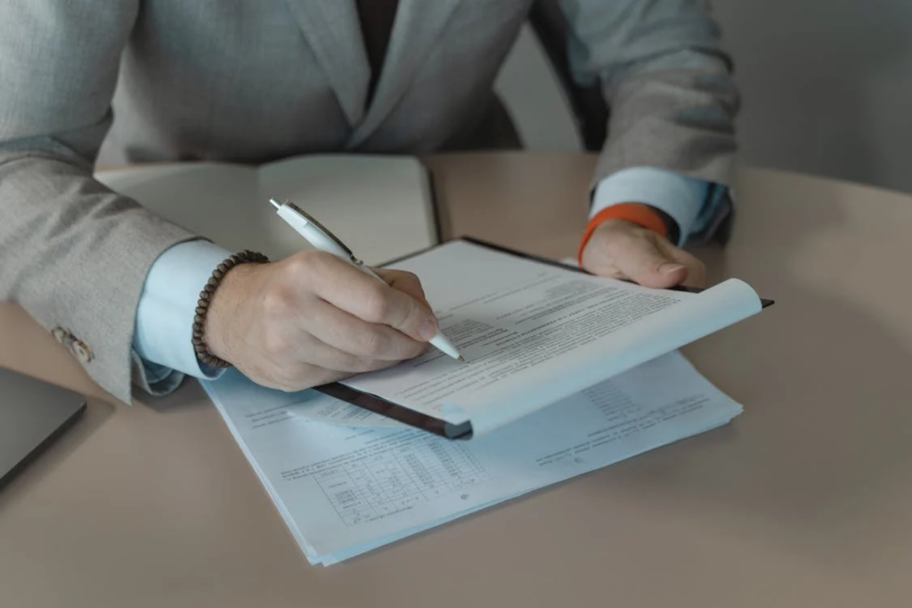 Person in gray suit holding white pen and document on a clipboard