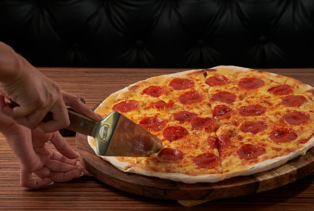 Fresh pepperoni pizza being sliced, highlighting delicious cheese and toppings.