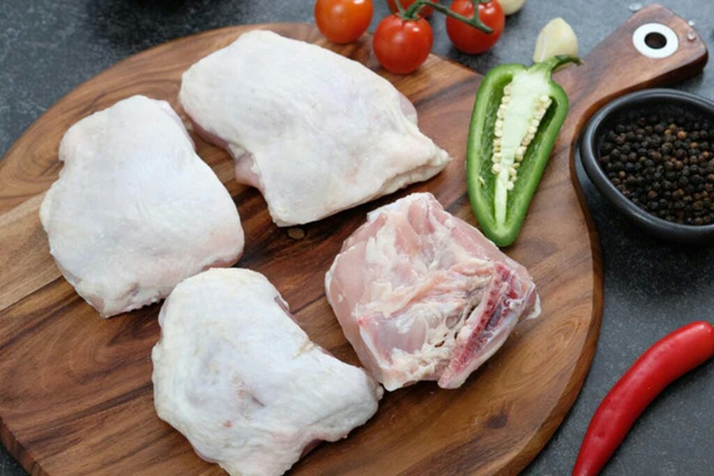 Raw chicken pieces with vegetables on a wooden board
