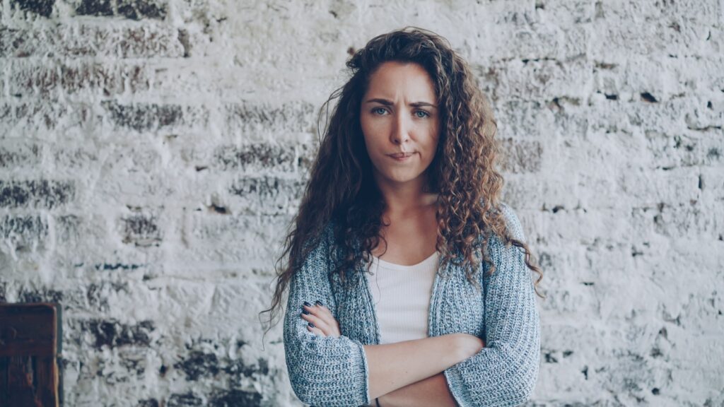 Woman with curly hair standing with arms crossed.