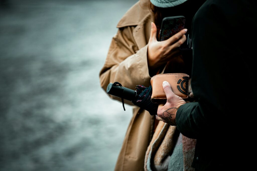 Two people holding phones and a wallet outdoors.