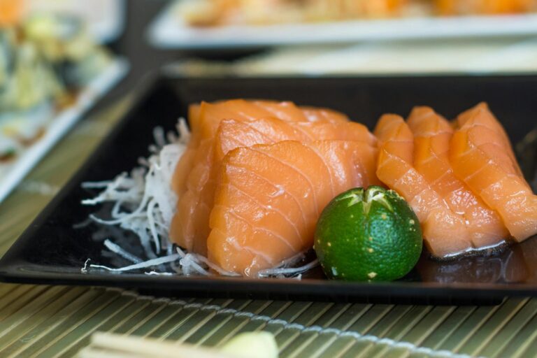 Close-up of fresh salmon sashimi served with calamansi on a black plate.