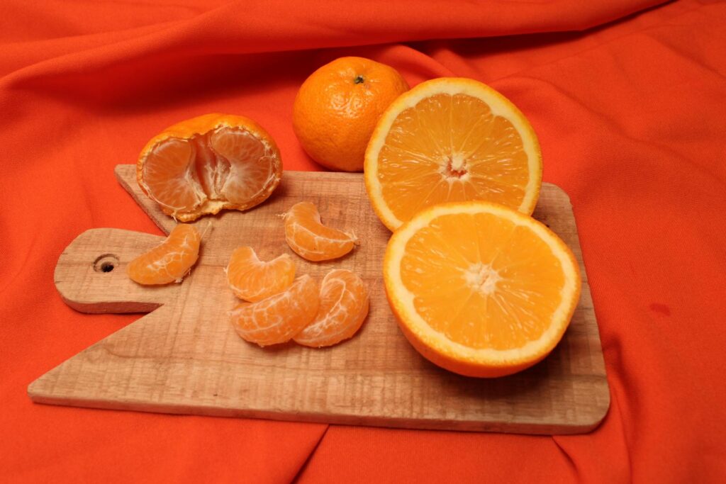 Sliced oranges and tangerines on a wooden tray with vibrant orange background.