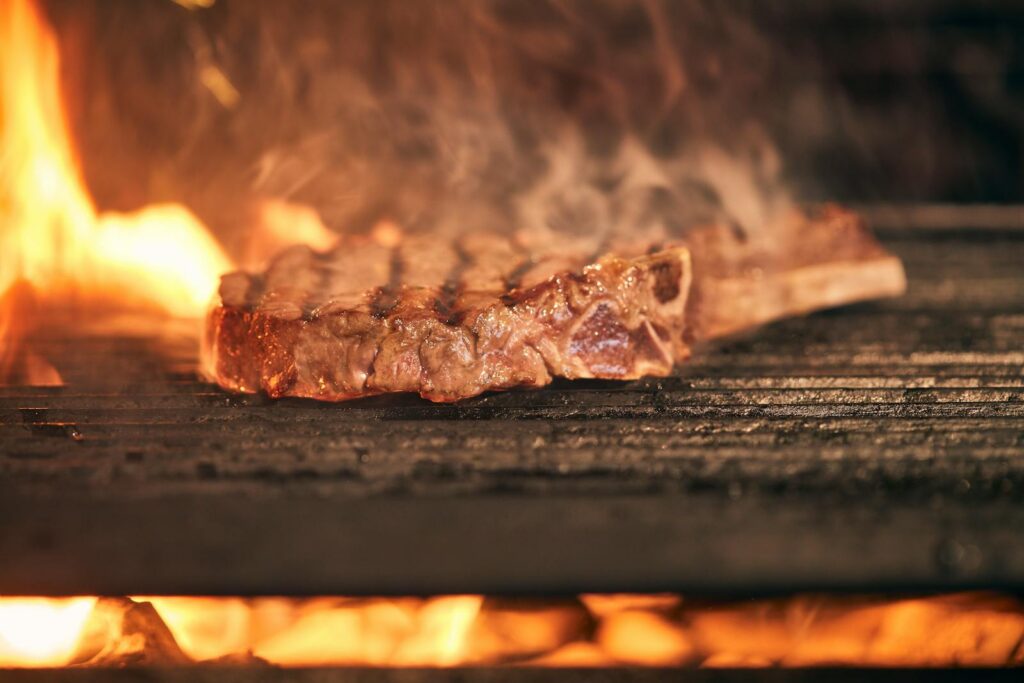Close-up of a delicious steak being grilled over an open flame, emitting a mouth-watering aroma.