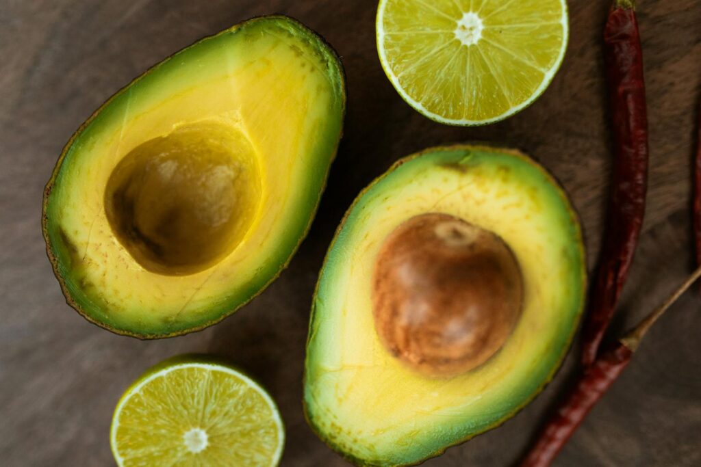 Sliced avocado and lime with chili peppers on a wooden background, perfect for culinary themes.