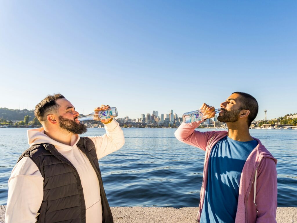 a couple of men standing next to each other drinking water