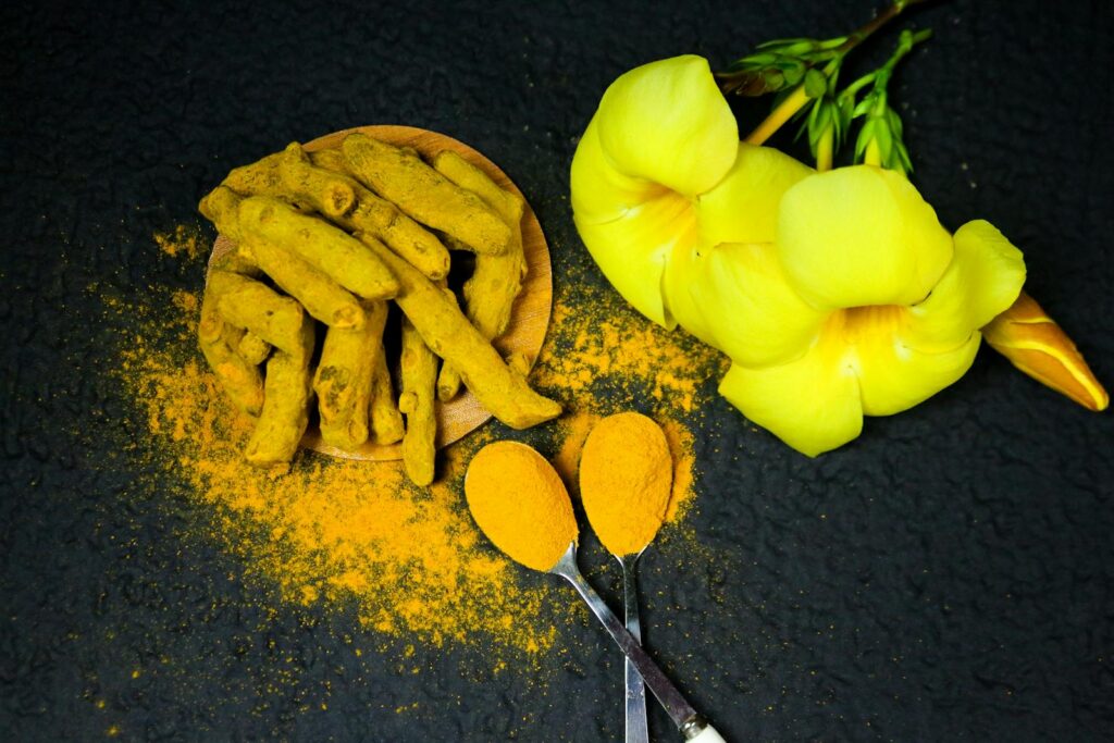 Close-up of turmeric roots, powder, and yellow bell flowers on a black background.