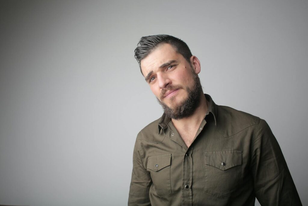 Close-up portrait of a young man with a beard, expressing thoughtfulness in a studio setting.