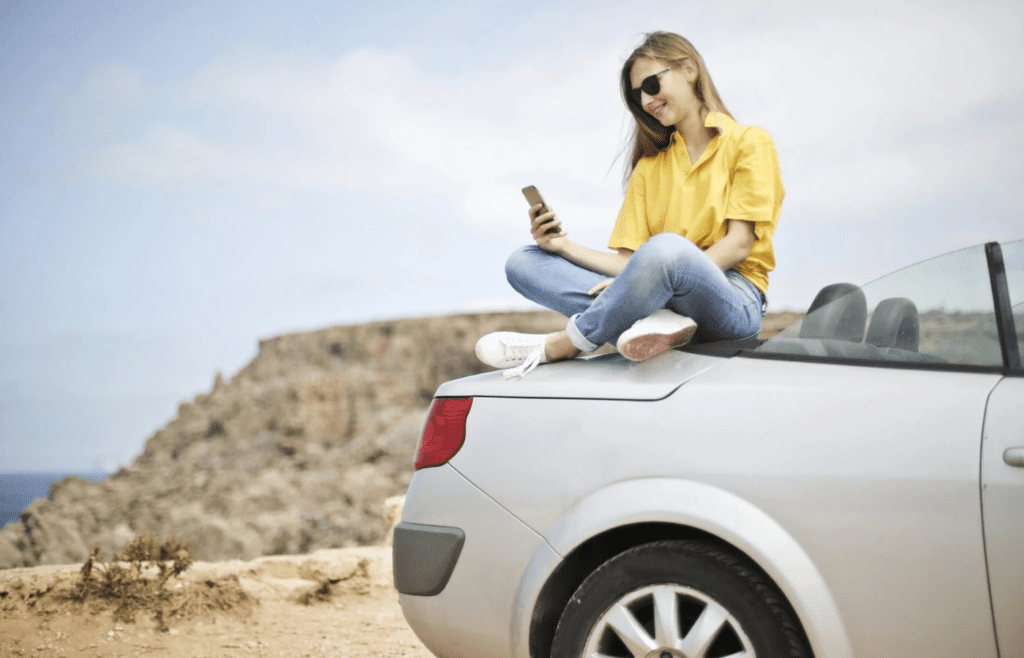 woman on top of car looking at phone