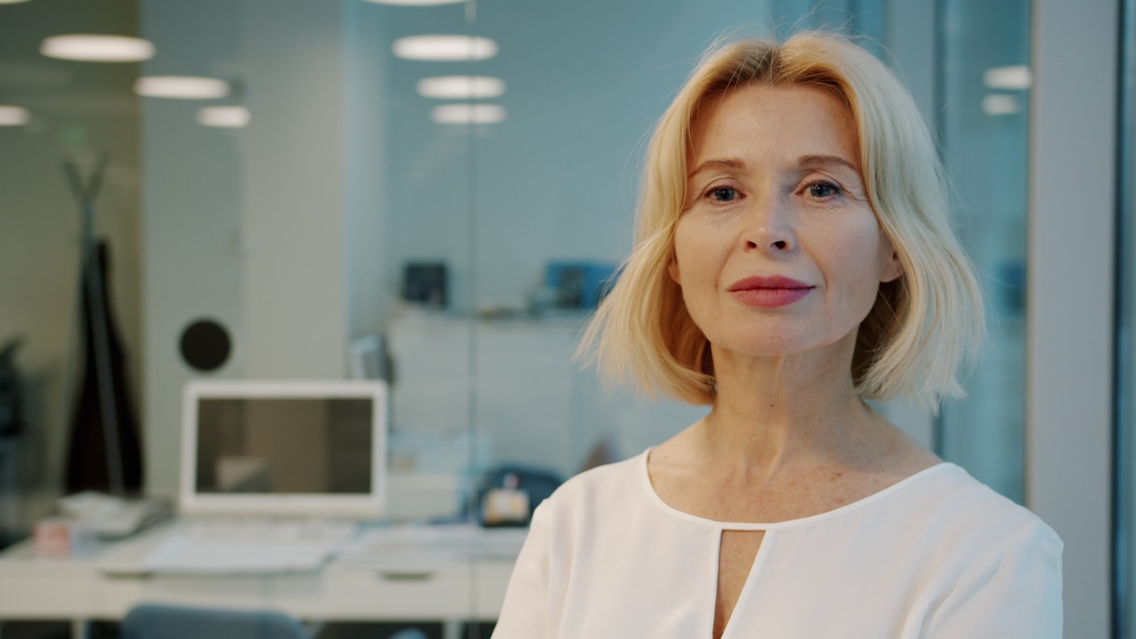 A blonde woman in a white blouse smiles