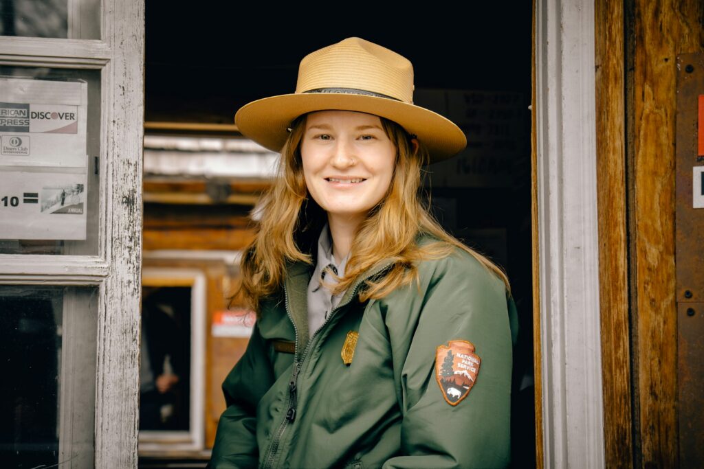 Smiling park ranger woman in uniform standing in a doorway.