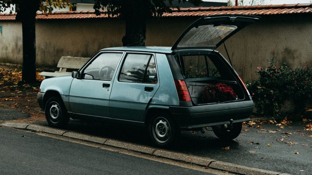 A classic hatchback car parked on a leafy street during the fall season.