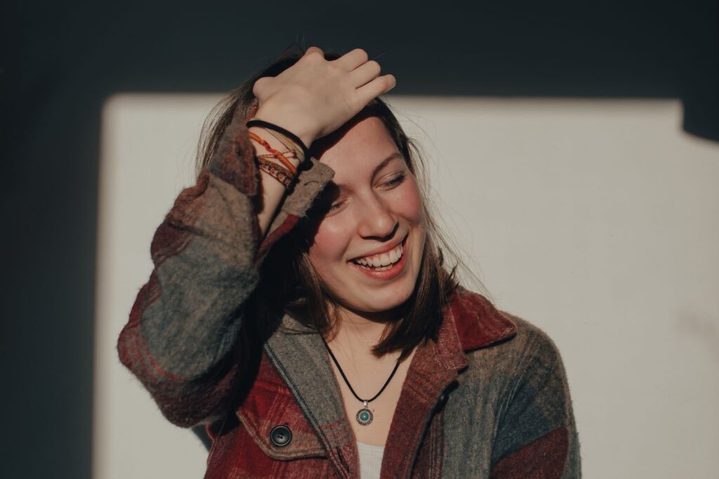 A joyful woman laughing and holding her head under natural sunlight indoors.