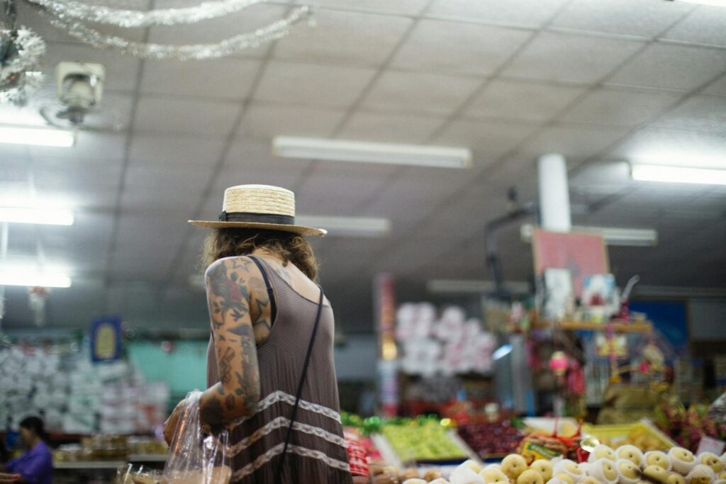 A tattooed woman browsing fruits at an indoor market stall.