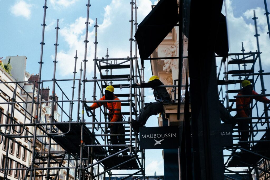 Silhouetted construction workers on scaffolding in an urban environment under blue skies.