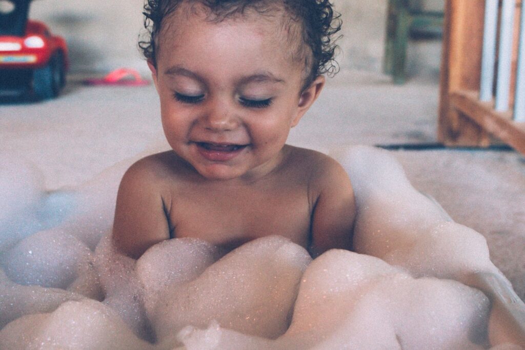 Candid shot of a smiling baby enjoying a bubble bath indoors, captured in a warm and playful atmosphere.