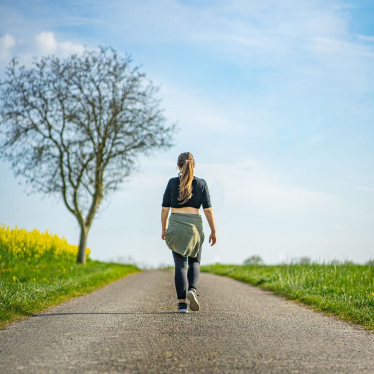 A woman walks along a rural path under a clear blue sky, experiencing the tranquility of nature.