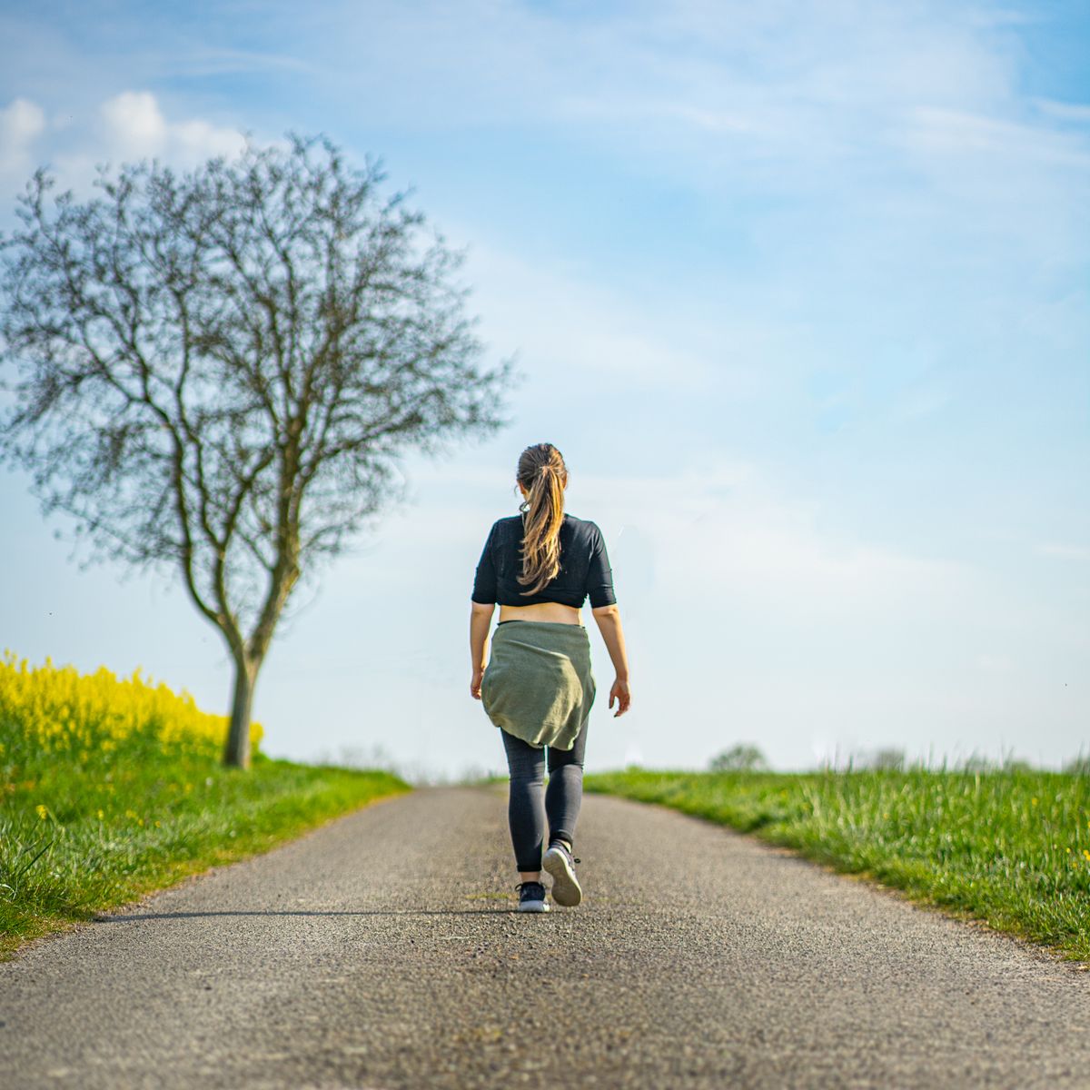 A woman walks along a rural path under a clear blue sky, experiencing the tranquility of nature.