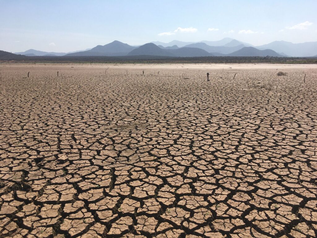 A vast, cracked earth landscape under clear skies depicting severe drought conditions.