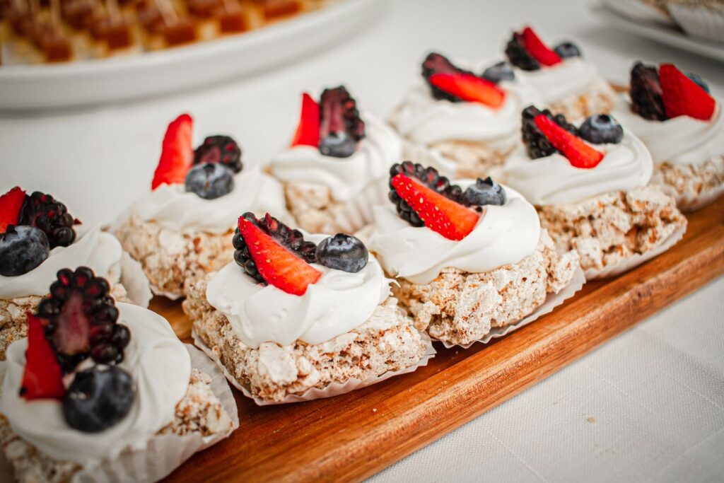 Close-up of berry-topped desserts with whipped cream on a wooden tray, perfect for a sweet indulgence.