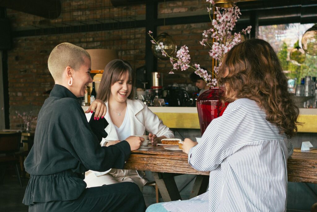 Three women laughing and enjoying dessert together in a cozy café setting.