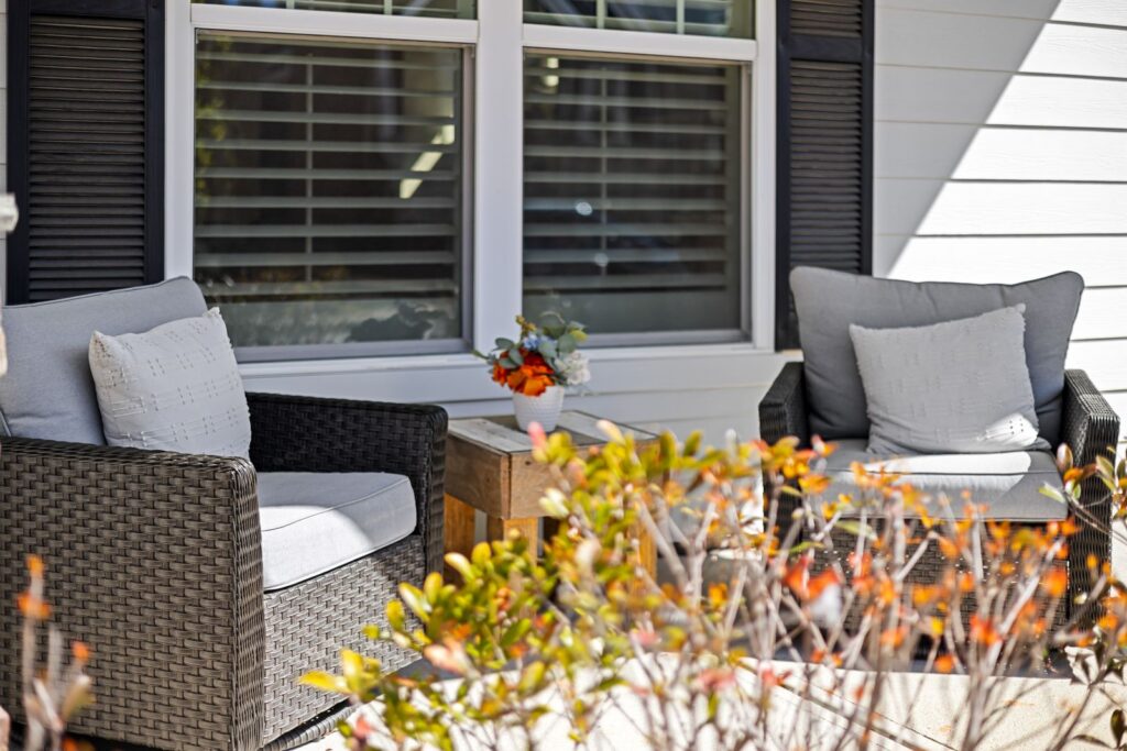 Outdoor patio scene featuring wicker armchairs and plants in vibrant sunlight.