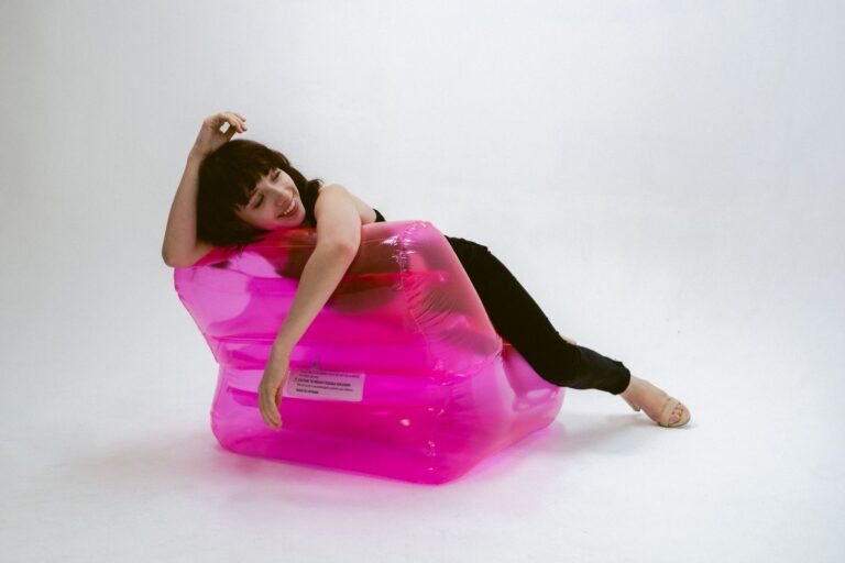 Stylish woman posing on a bright pink inflatable chair indoors.