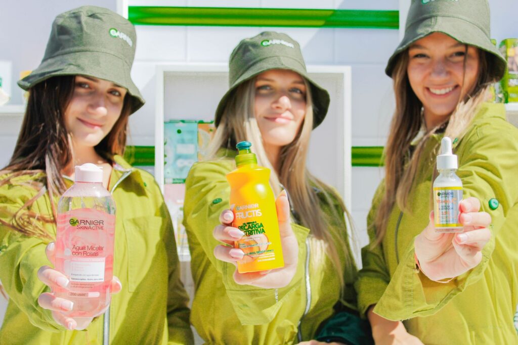 Three women showcasing Garnier skincare products with joyful expressions outdoors.