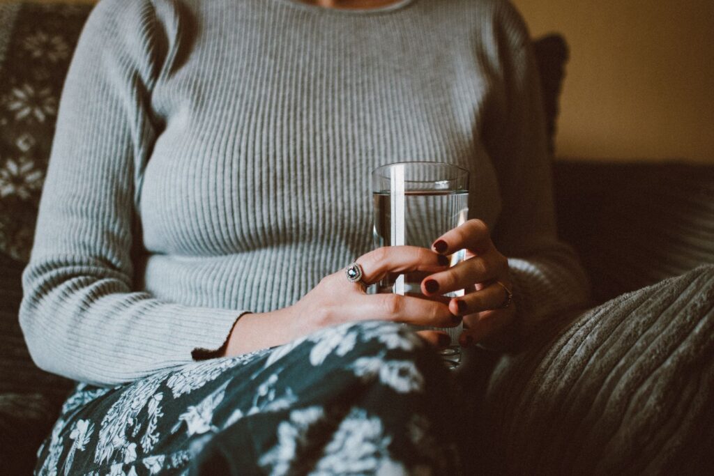 Close-up of a woman holding a glass of water while sitting indoors, conveying calm and relaxation.