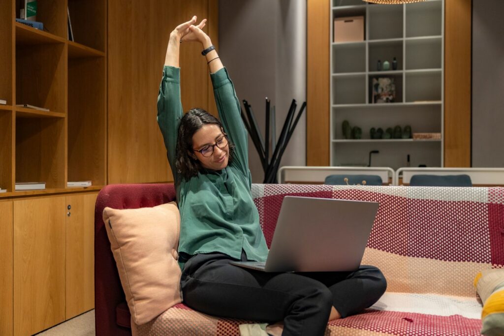 A woman relaxes while working from home on a sofa, showcasing a flexible work environment.