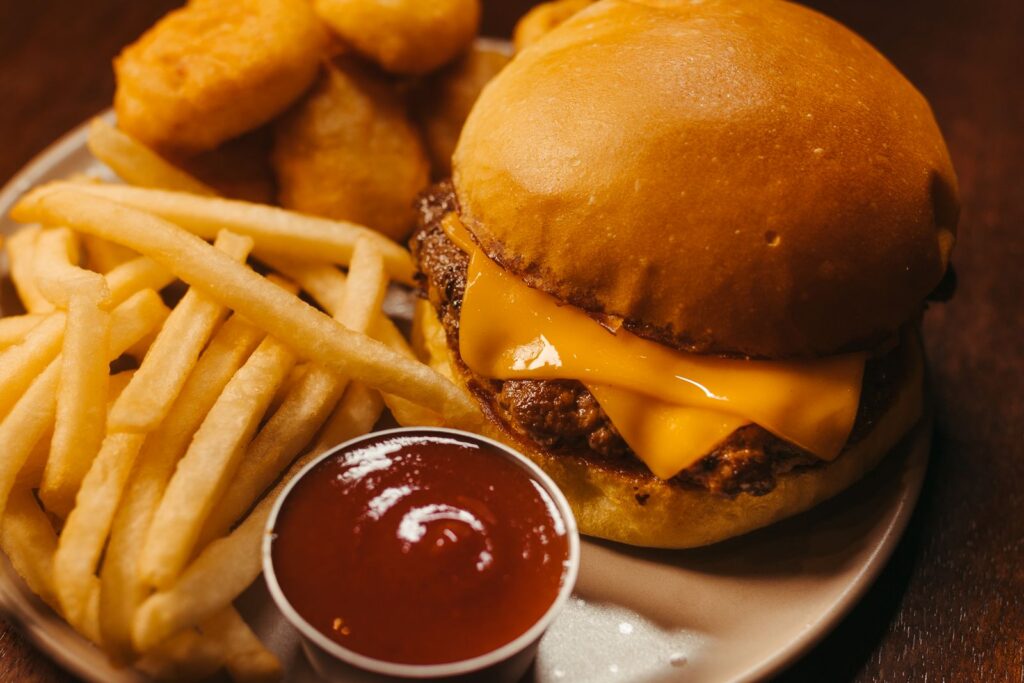 Close-up of a cheeseburger with french fries, nuggets, and ketchup on a plate.
