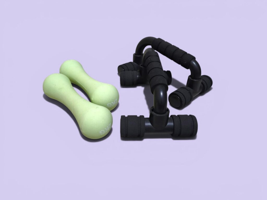 Two green dumbbells and black push-up bars on purple background.