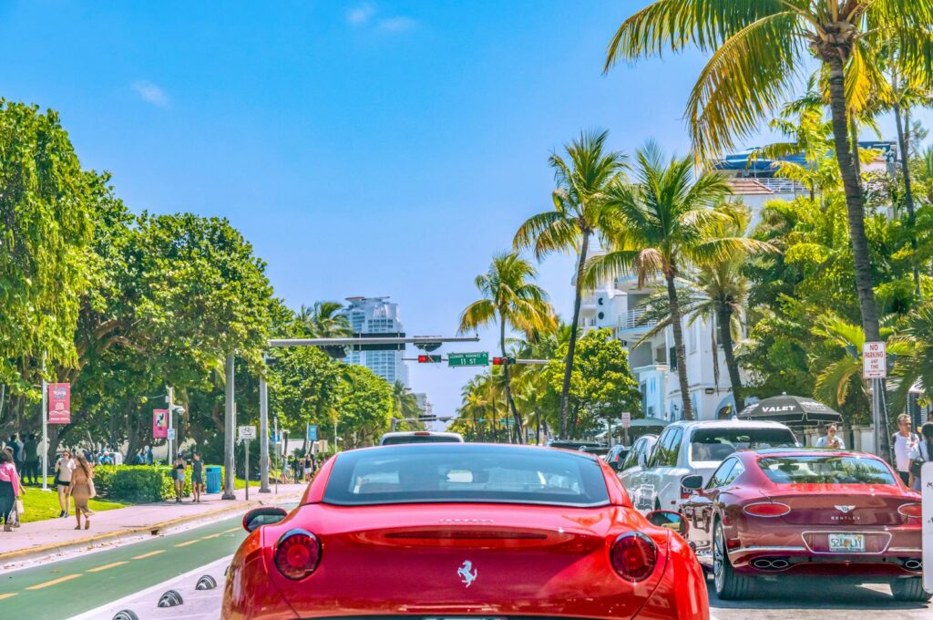Colorful scene on Miami Beach's streets filled with luxury cars, palm trees, and bright sunlight.