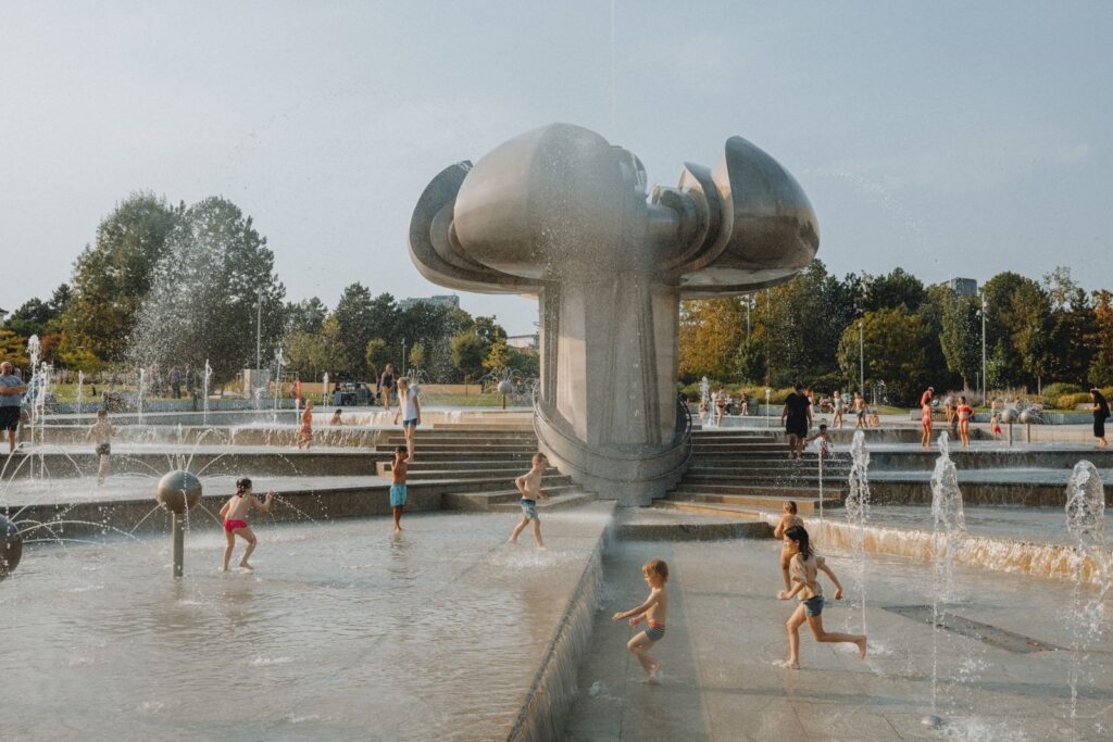 Children enjoying a summer day playing at a modern architectural fountain in a city park.