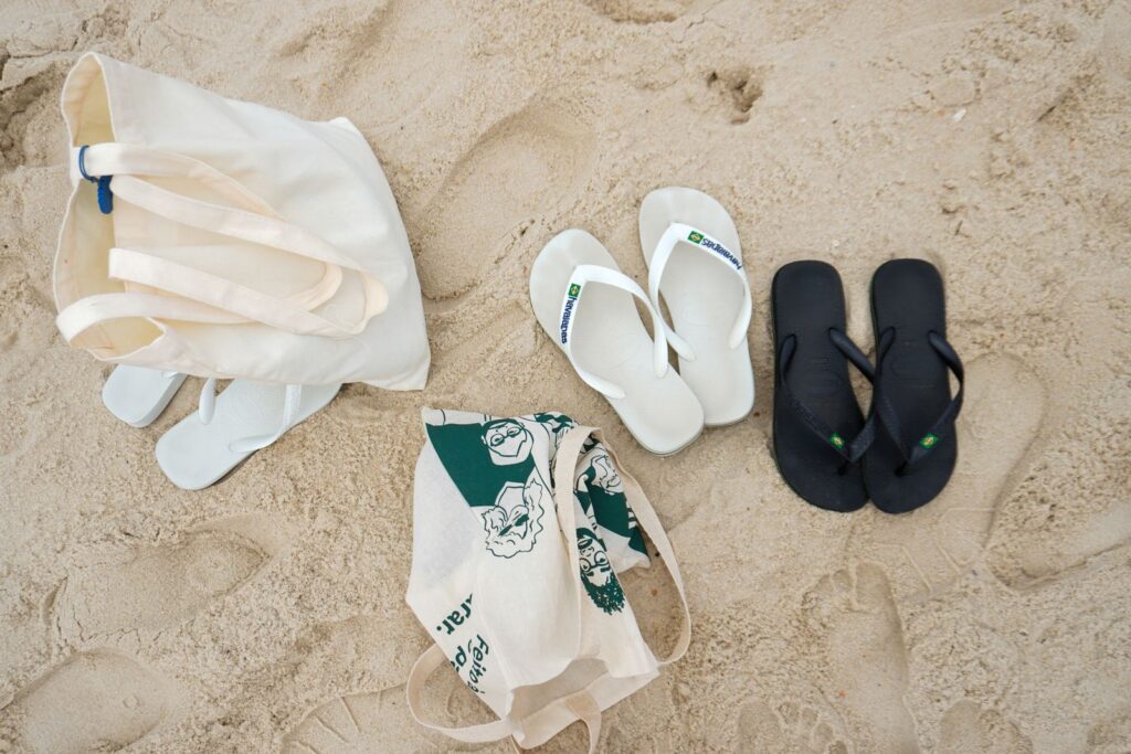 Flat lay of sandals and a tote bag on a sandy beach, ideal for summer themes.