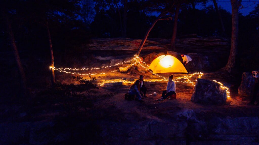 A cozy campsite illuminated by string lights and a glowing tent under a night sky.
